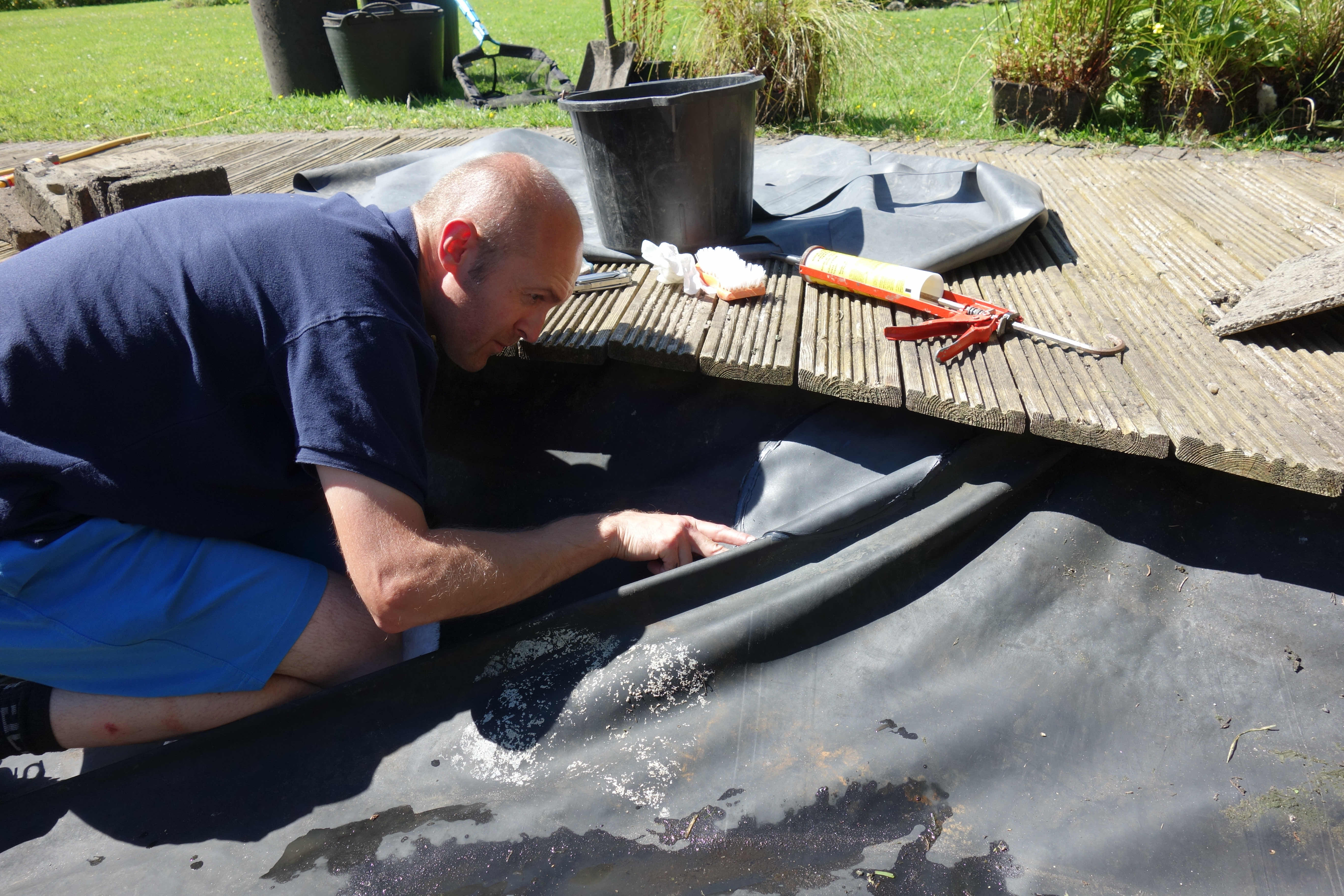 Pond contractor repairing a damaged pond liner, during a pond maintenance visit in Clitheroe.